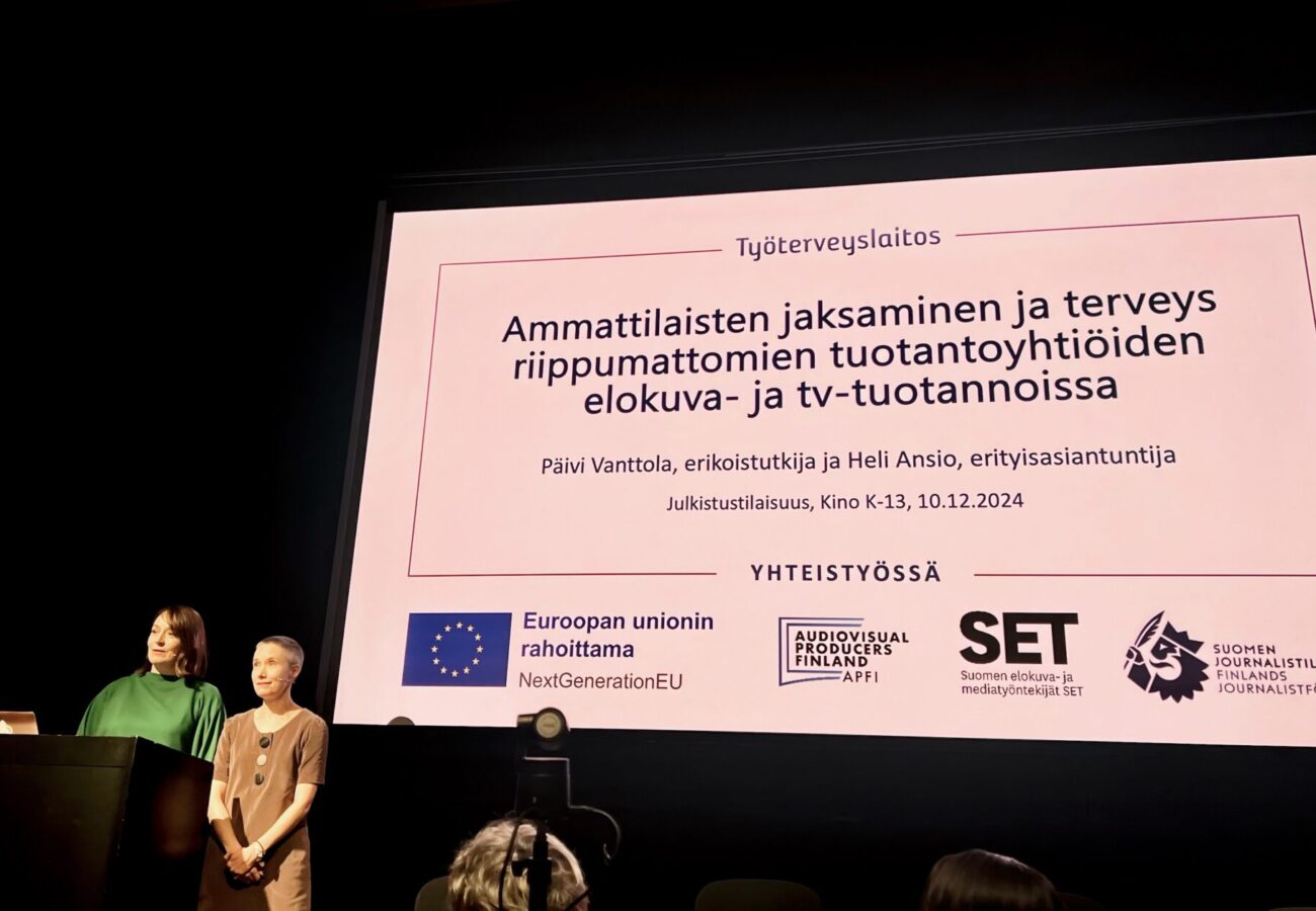 Työterveyslaitoksen tutkijat Päivi Vanttola ja Heli Ansio. seisovat presentaation edessä.